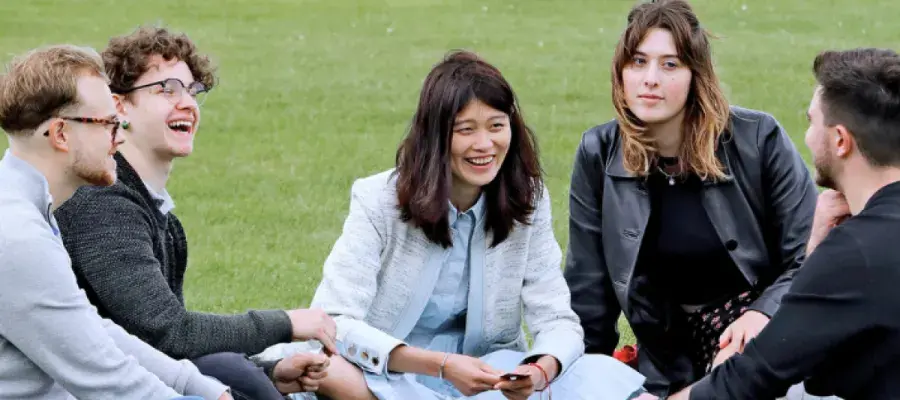 A group of five students six on the grass, talking and laughing